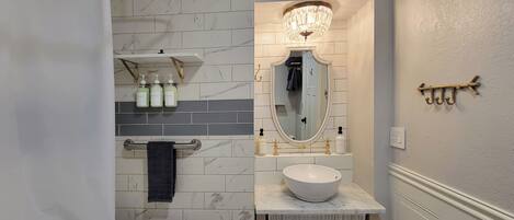 A bathroom with a white toilet, a sink with a marble countertop, a mirror with a gold frame, and a chandelier above the mirror.