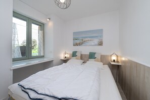 A bedroom with a bed, a window, a painting, and two bedside lamps.
