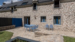 Un bâtiment en pierre doté d’un patio comprenant une table et des chaises.