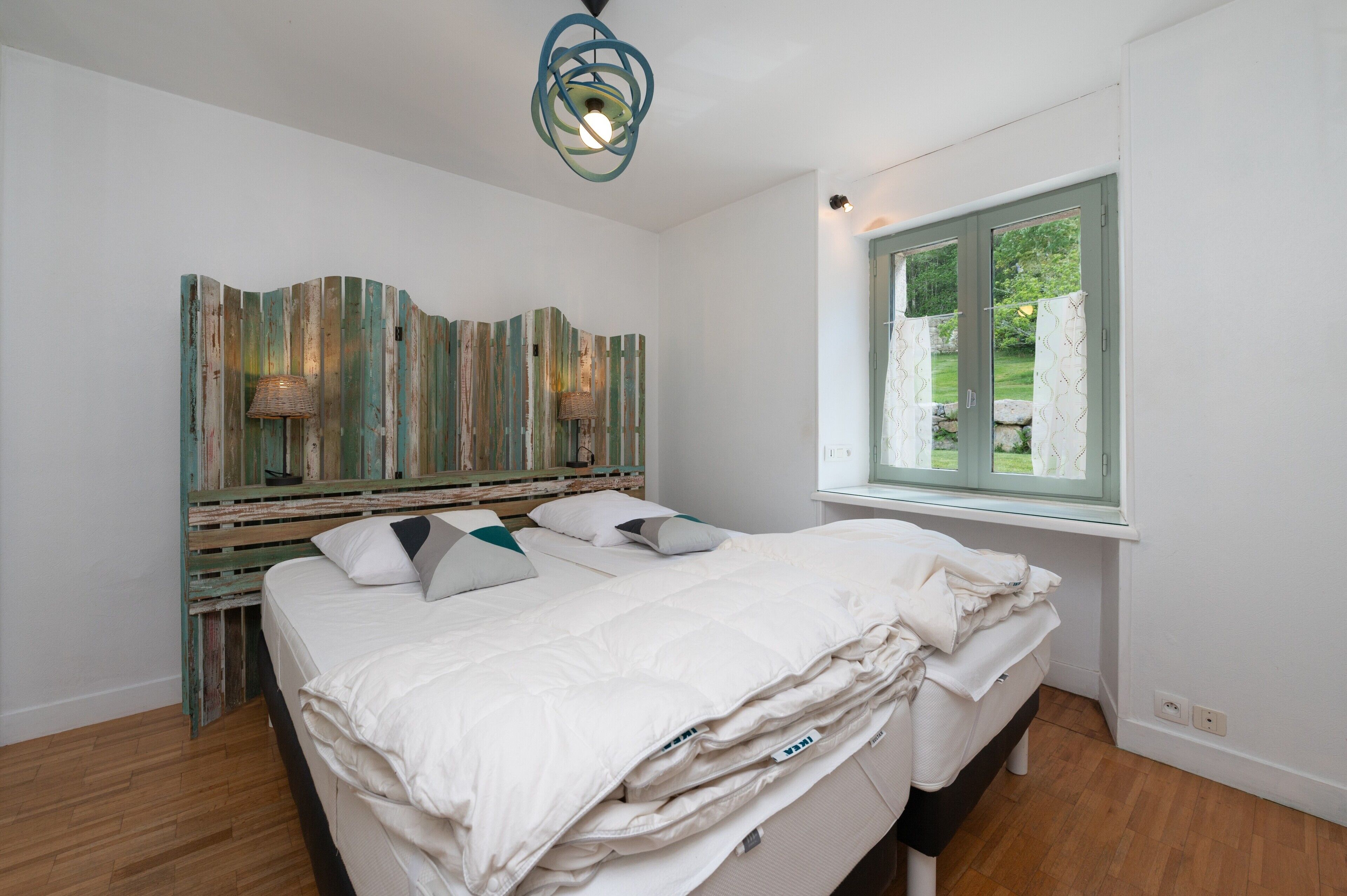 A bedroom with a bed, a window, a wall-mounted lamp, and a ceiling light fixture.