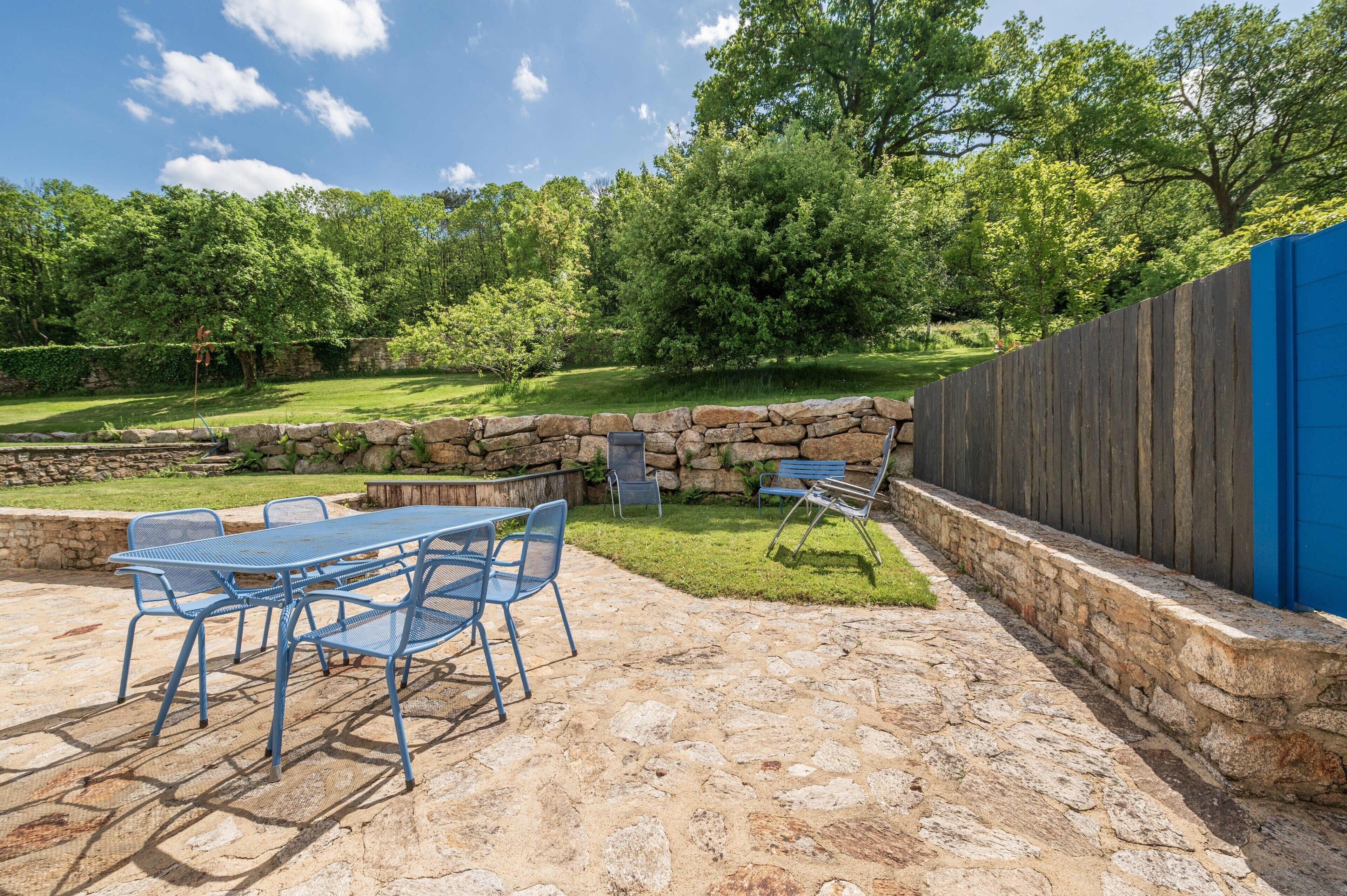 A patio with a stone table and chairs, a stone wall, and a wooden fence.
