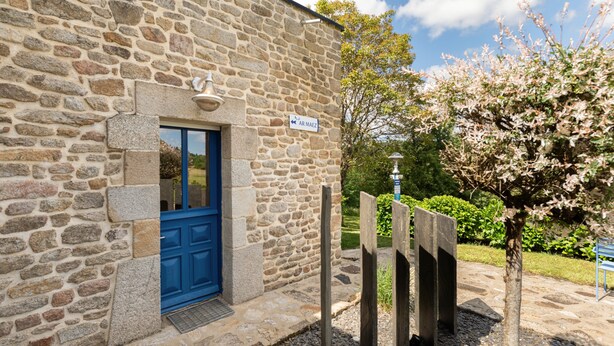 Un bâtiment en pierre avec une porte bleue, une enseigne indiquant « AR MAEZ » et une clôture en bois.
