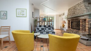 Une pièce avec une cheminée en pierre, un canapé agrémenté de coussins à motifs, un fauteuil jaune, une petite table et une chaise.