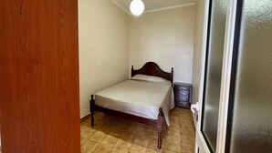 A small bedroom with a wooden bed, a bedside table, and a window with blinds. - Sea View Madeira Machico 1 Bedrooms Terrace Villa (Machico)