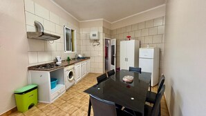 A compact kitchen with a dining area, including a stove, sink, washing machine, cabinets, and a refrigerator. - Sea View Madeira Machico 1 Bedrooms Terrace Villa (Machico)