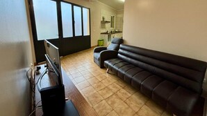 A living room with a sofa, a TV, and a kitchen in the background. - Sea View Madeira Machico 1 Bedrooms Terrace Villa (Machico)