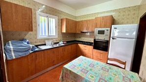 A compact kitchen with wooden cabinets, a gas stove, an oven, a microwave, and a refrigerator. - Sea View Madeira Machico 2 Bedrooms Terrace Villa (Machico)