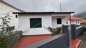 A modern two-story house with a red-tiled roof, a small front porch, and a red brick pathway leading to the entrance. - Sea View Madeira Machico 2 Bedrooms Terrace Villa (Machico)