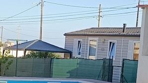 Ein Schwimmbecken mit Holzterrasse, umgeben von einem grünen Zaun und einem Haus im Hintergrund.