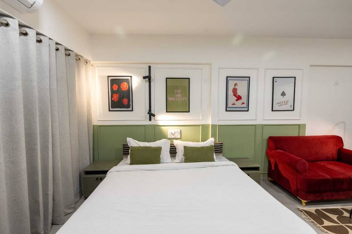 A hotel room with a bed, green headboard, a red armchair, and framed pictures on the wall.