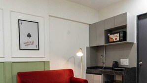 A compact living space with a red sofa, a small round table, a patterned rug, a ceiling fan, and a kitchenette. - House of KP  (Pune)