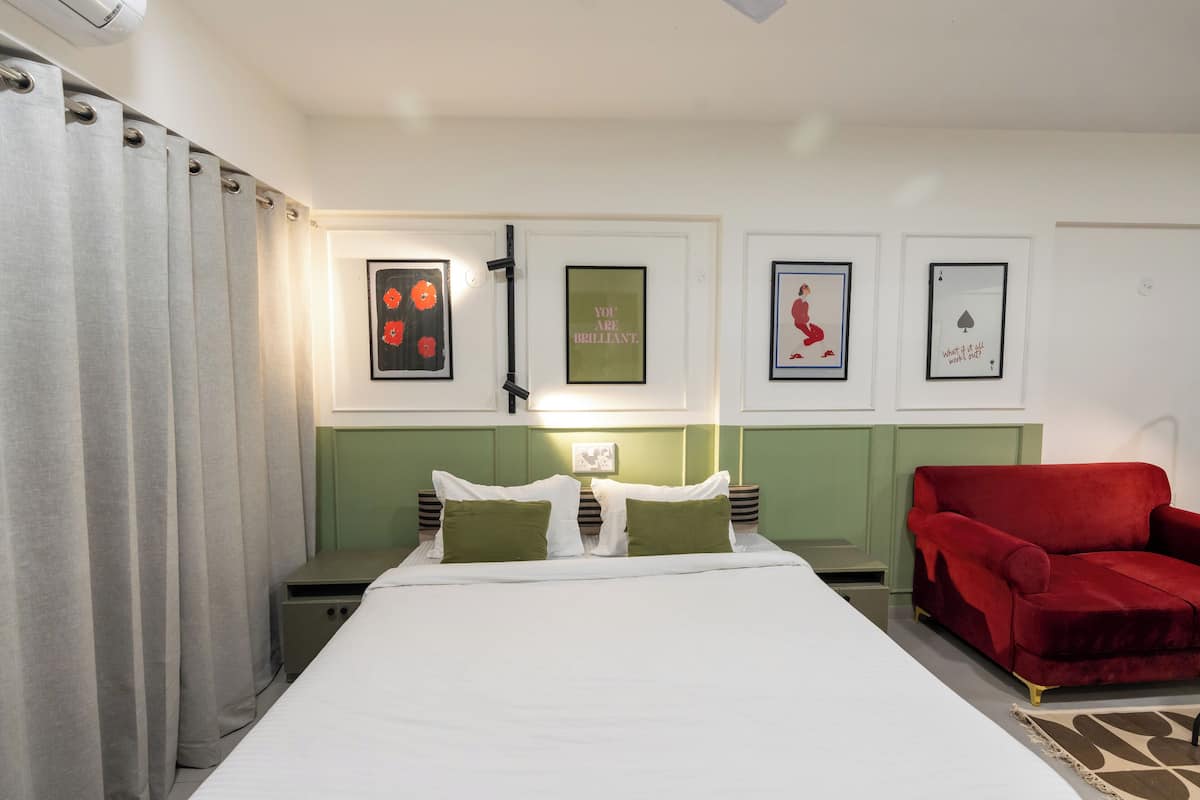 A neatly arranged bedroom with a bed, two bedside tables, a red armchair, and wall-mounted artwork.
