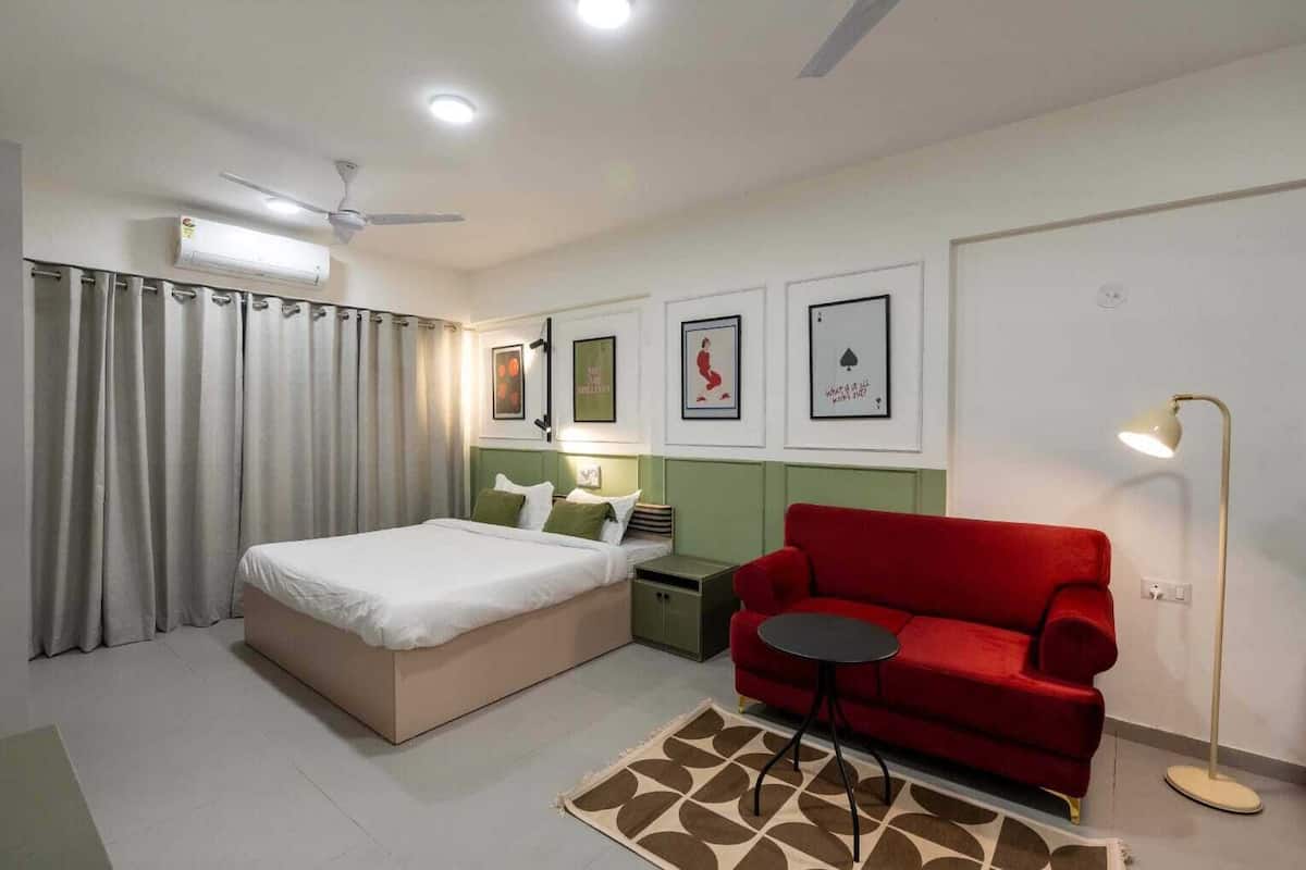 A hotel room with a bed, a red sofa, a small table, a floor lamp, and a ceiling fan.