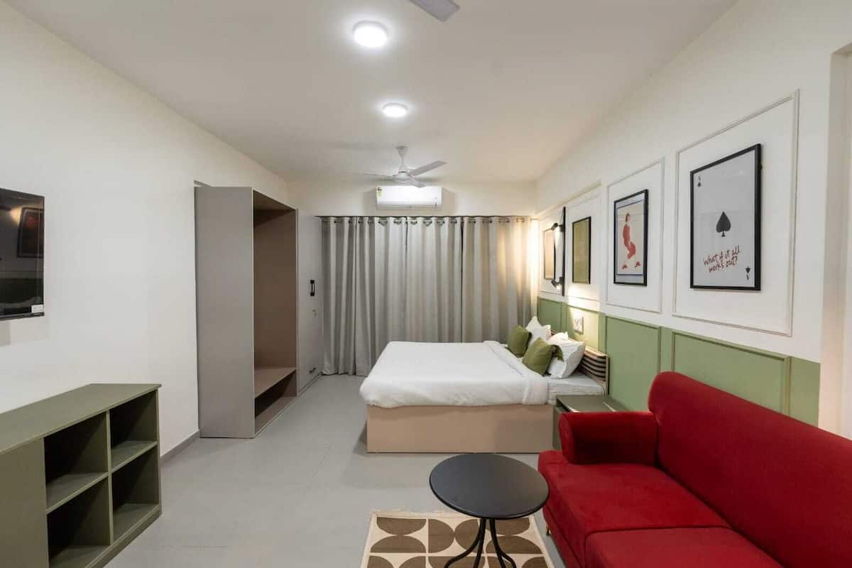 A modern hotel room with a bed, a red sofa, a small table, and a TV on the wall.