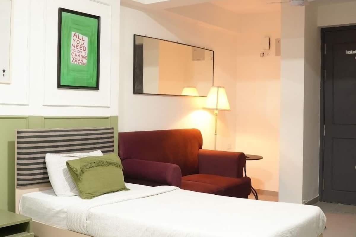 A bedroom with a bed, a nightstand, a red chair, a lamp, and a mirror on the wall.