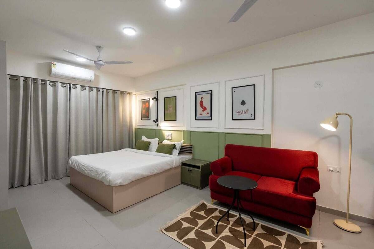 A hotel room with a bed, a red sofa, a small table, a floor lamp, and a ceiling fan.