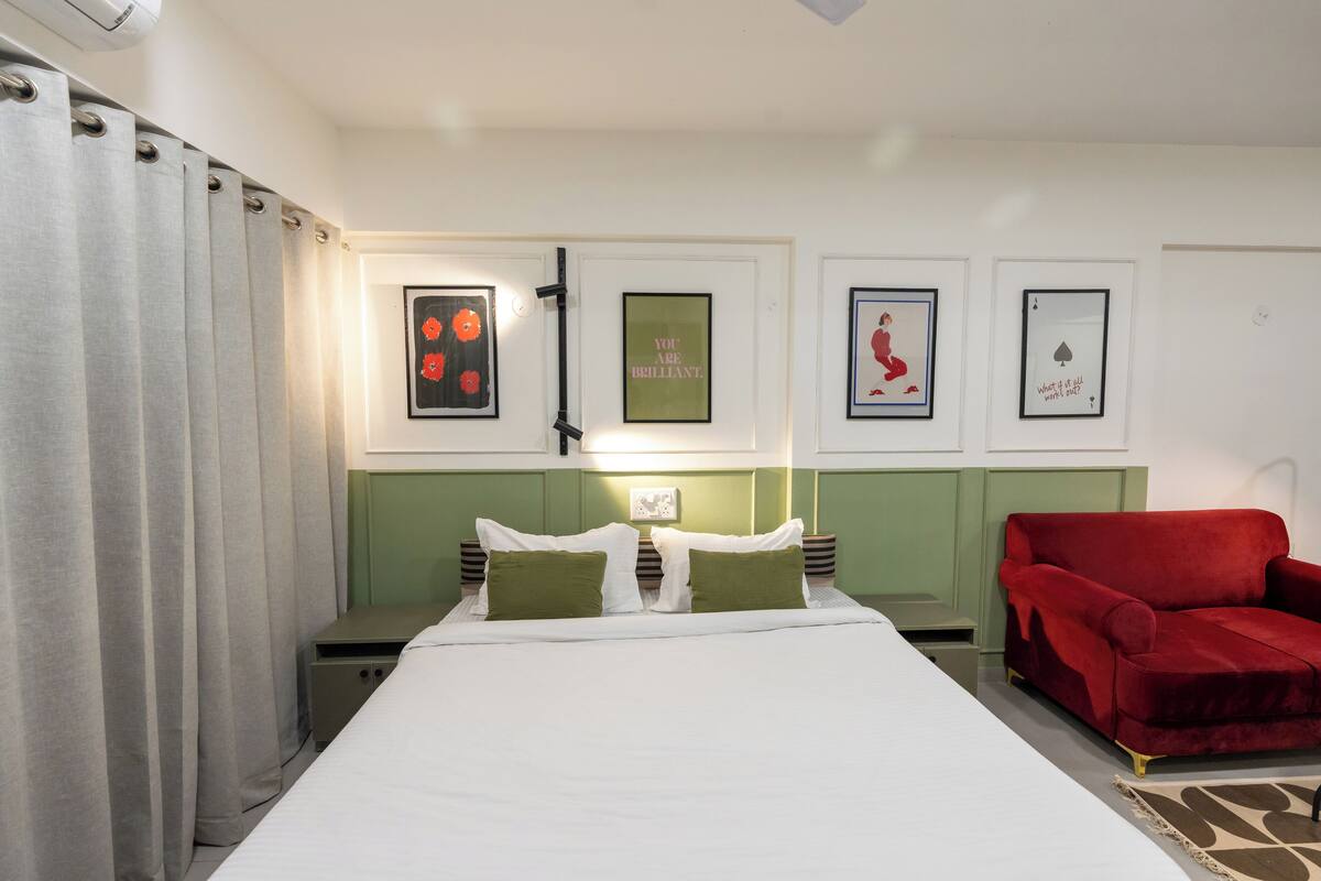 A neatly arranged bedroom with a bed, two bedside tables, a red armchair, and wall-mounted artwork.