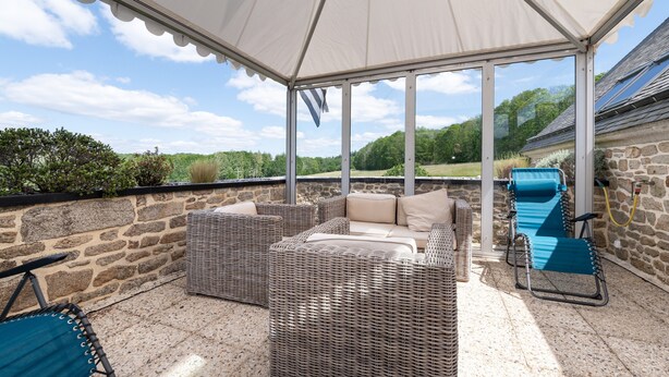 A covered patio area with wicker furniture, a bicycle, and a stone wall. - Guest Room “A L’abri - An Douar La Terre” with Shared Terrace, Garden, and Wi-Fi (Saint-Nolff)