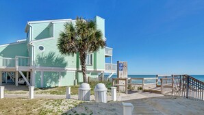 Una propietat a peu de platja amb una estructura de diversos nivells, una palmera i un camí de fusta cap a la platja.
