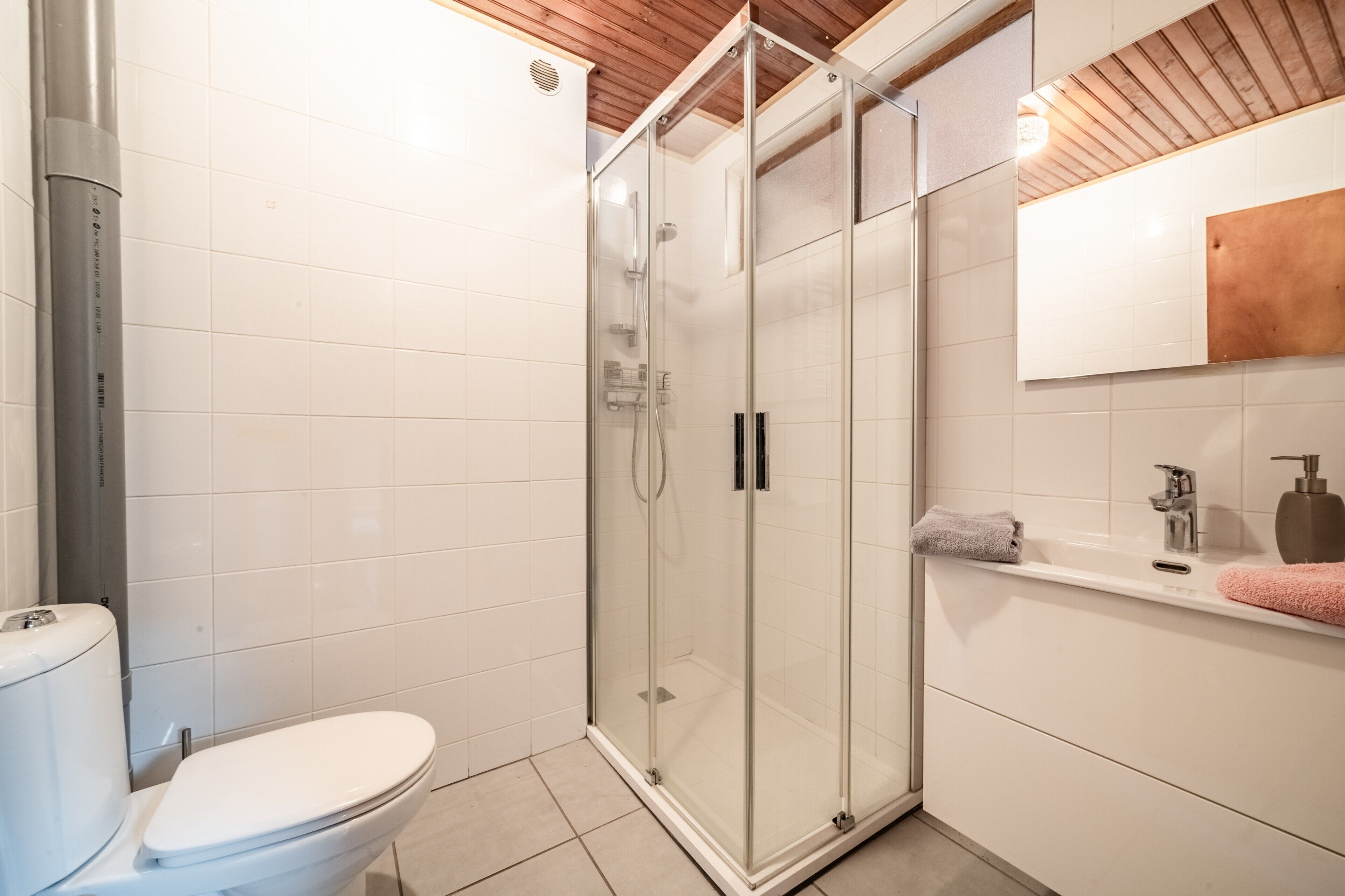 Ein modernes Badezimmer mit einer gläsernen Duschkabine, einer weißen Toilette und einem Waschbecken mit Seifenspender.