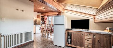 A kitchen with wooden cabinets, a refrigerator, a coffee maker, and a television on a wooden counter.