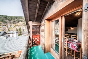 Een houten balkon met uitzicht op een dorp, een eethoek met een tafel en stoelen, en een houten deur.