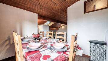 Een eethoek met een tafel voor vier personen, houten stoelen, een tafelkleed met dessin en een prullenbak.