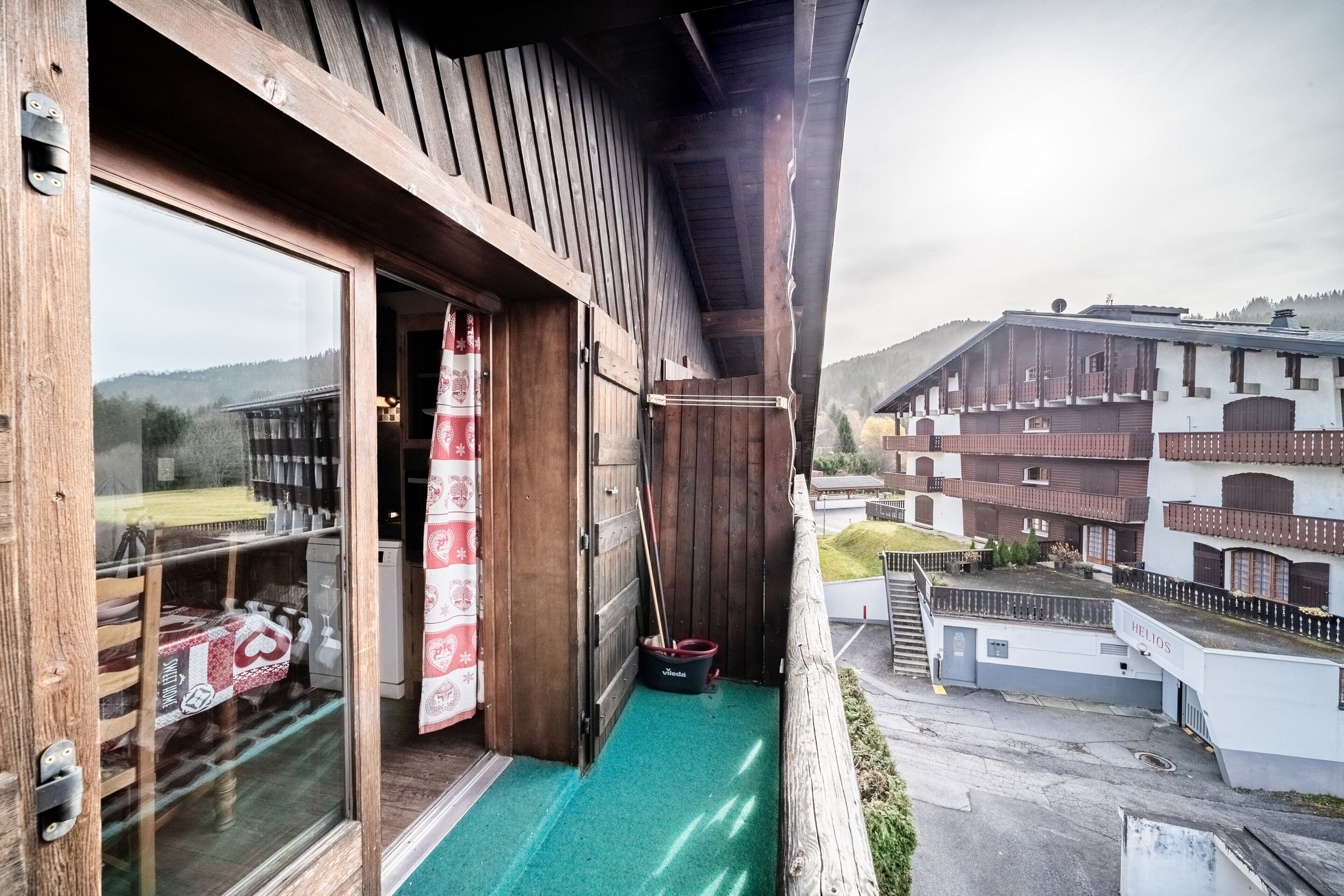 Ein Holzbalkon mit Bergblick, ein Fenster mit Vorhang und ein Wisch-Eimer.