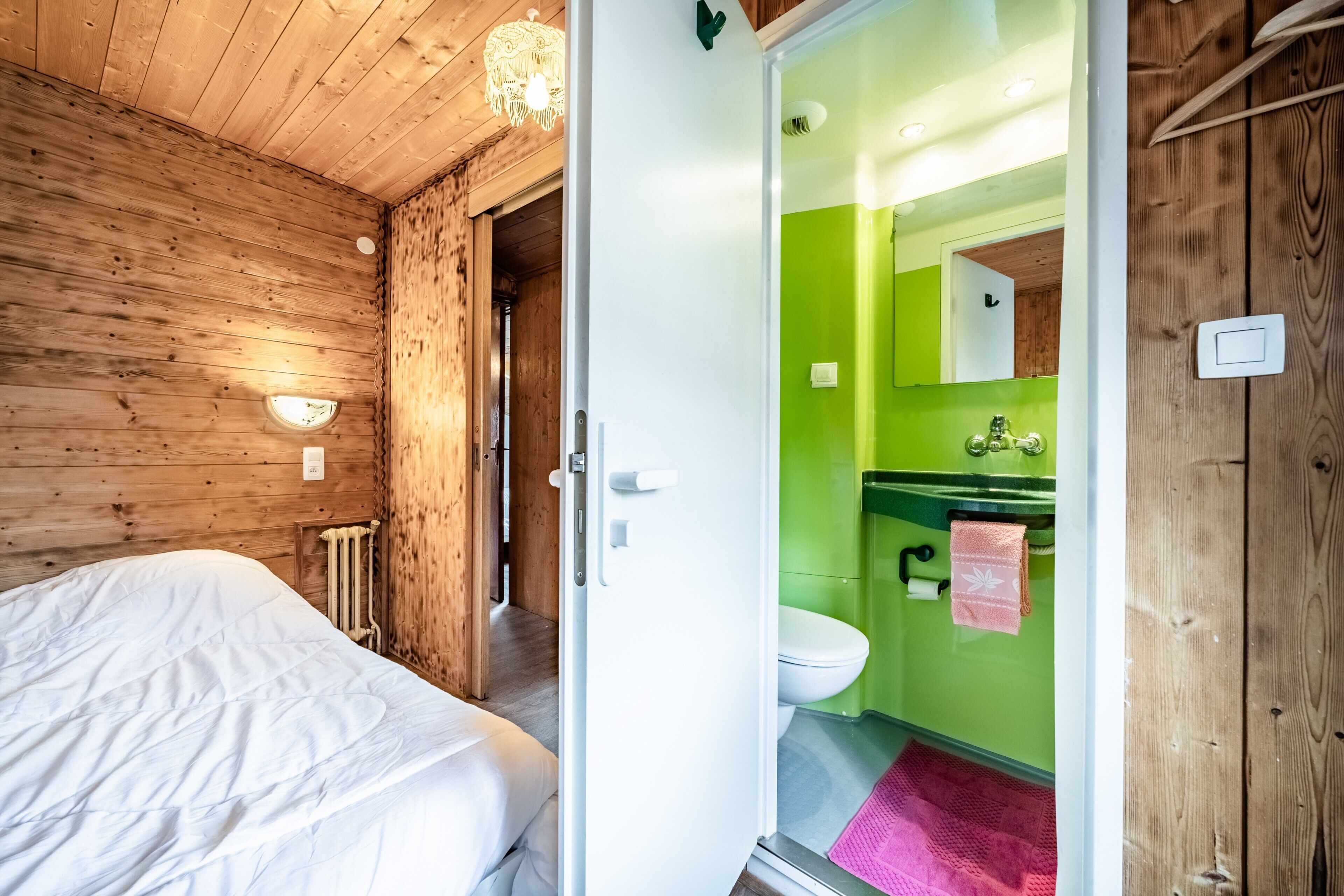 Ein Zimmer aus Holz mit einem Bett und einer Tür zu einem Badezimmer mit grüner Wand und weißer Toilette.