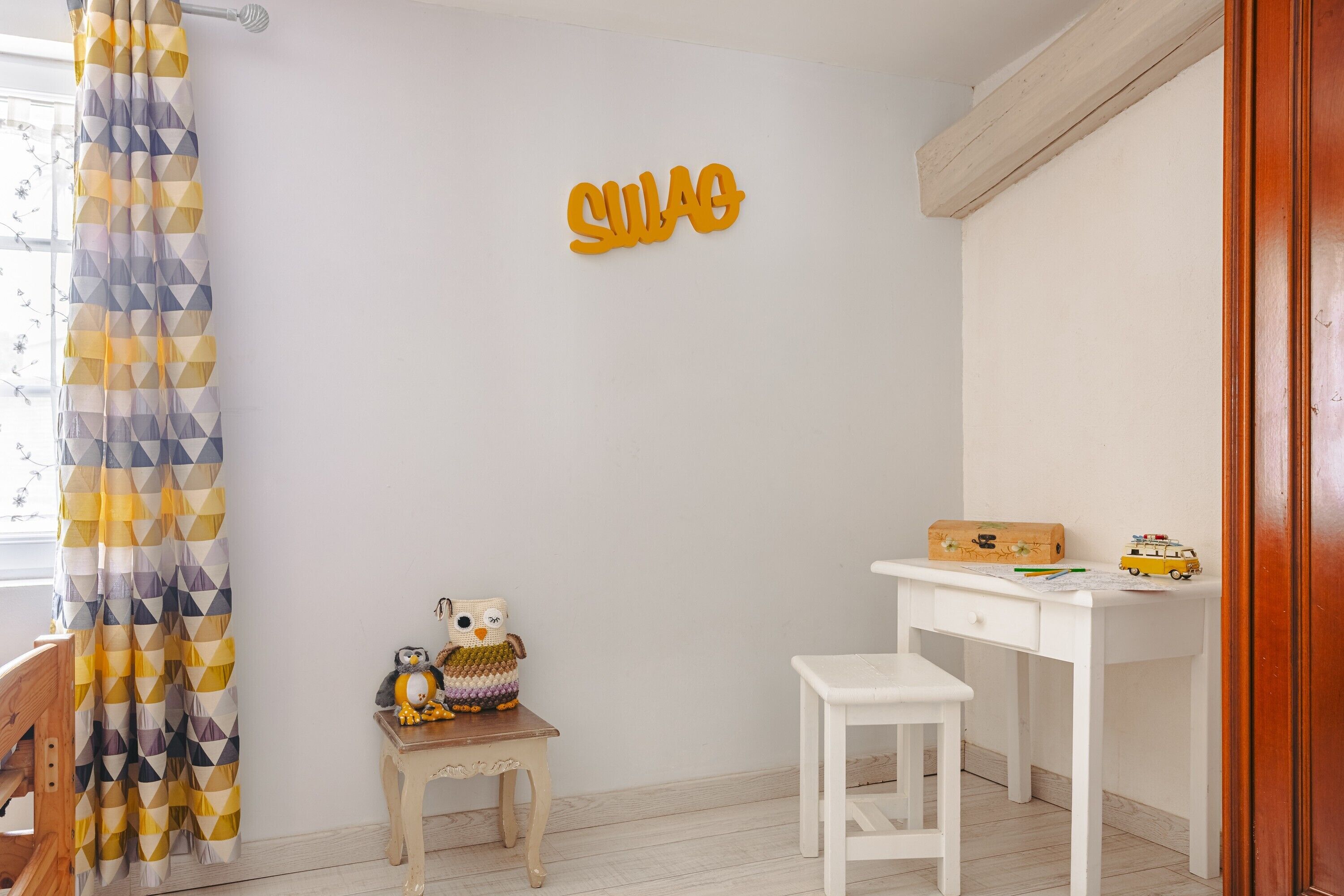 Une chambre d’enfant avec un bureau, une petite table, un jouet et un rideau à motifs géométriques.