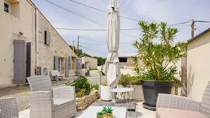 Eine Terrasse im Freien mit Korbmöbeln, einem Tisch, Kübelpflanzen und einem großen Sonnenschirm.