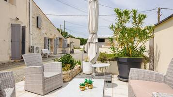 Eine Terrasse im Freien mit Korbmöbeln, einem Tisch, Kübelpflanzen und einem großen Sonnenschirm.