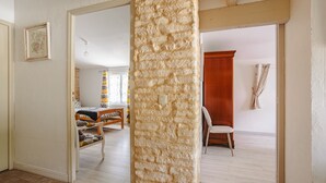 Ein Zimmer mit Säule aus Stein, einer Holzbank, einem Bett und einem Fenster mit Vorhängen.