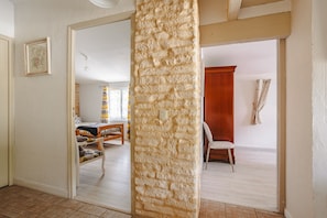 Una habitación con un pilar de piedra, un banco de madera, una cama y una ventana con cortinas.