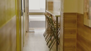 Un pasillo con suelo de madera, un vidrio al final y una fila de sillas a lo largo de la pared.