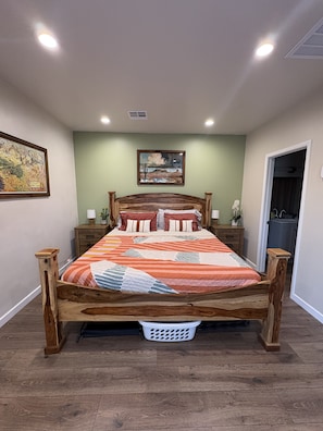 A bedroom with a wooden bed, green walls, a painting, and a door to a bathroom. - The Little Adobe - Daniel & Clara Boone Historic Bunkhouse in Central Phoenix! (Phoenix)