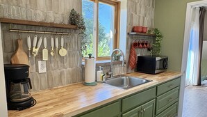 Una cocina con armarios verdes, una encimera de madera, una cafetera y una ventana con vistas a la vegetación.