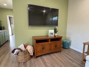 Una sala de estar con un televisor de pantalla plana montado en la pared, un mueble de madera para entretenimiento, una cesta tejida y una pequeña planta.