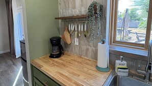 Una cocina con encimera de madera, armarios verdes, un lavabo de acero inoxidable y una ventana con vistas al exterior.