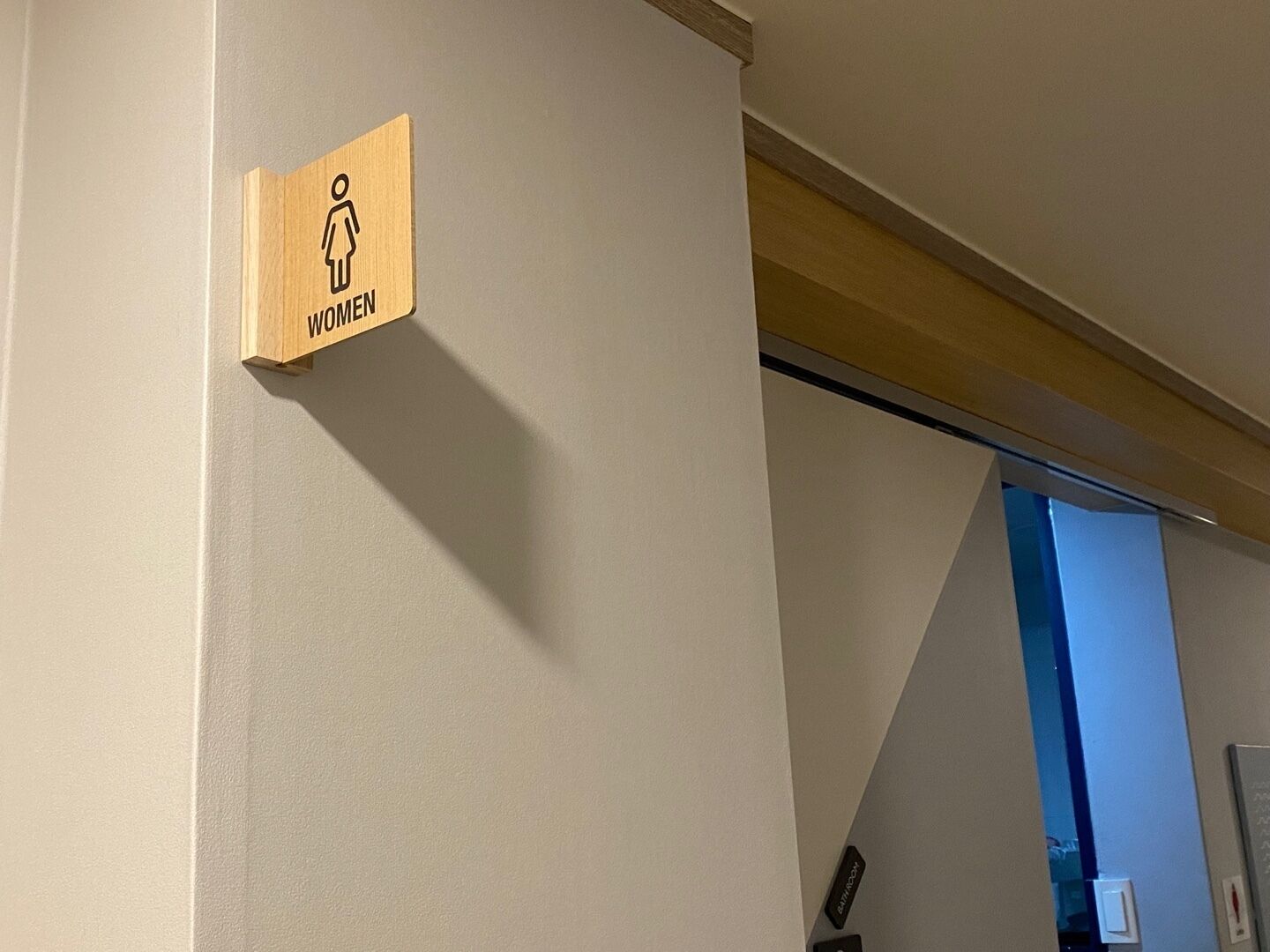 Un letrero de madera con el símbolo femenino y la palabra 'WOMEN', que indica el baño de mujeres.