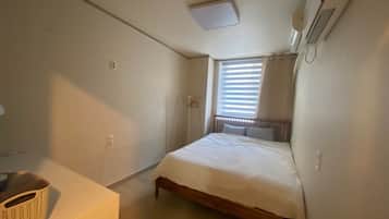 A small, clean room with a single bed, a bedside table, and a window with blinds.