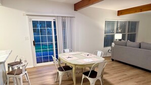 Ein Essbereich mit Tisch, Stühlen, einer Couch und einem Fenster mit Jalousien.