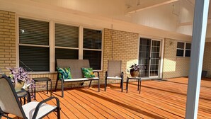 Eine überdachte Terrasse im Freien mit Holzdeck, einer Sitzecke mit Stühlen und einer Bank sowie einem Blumentopf.