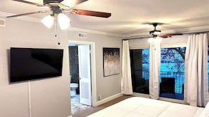A bedroom with a large bed, a ceiling fan, a TV, and a view of the outdoors. - Spacious  2BD Condo  HWY360/30  Grand Prairie (GP22B) (Grand Prairie)