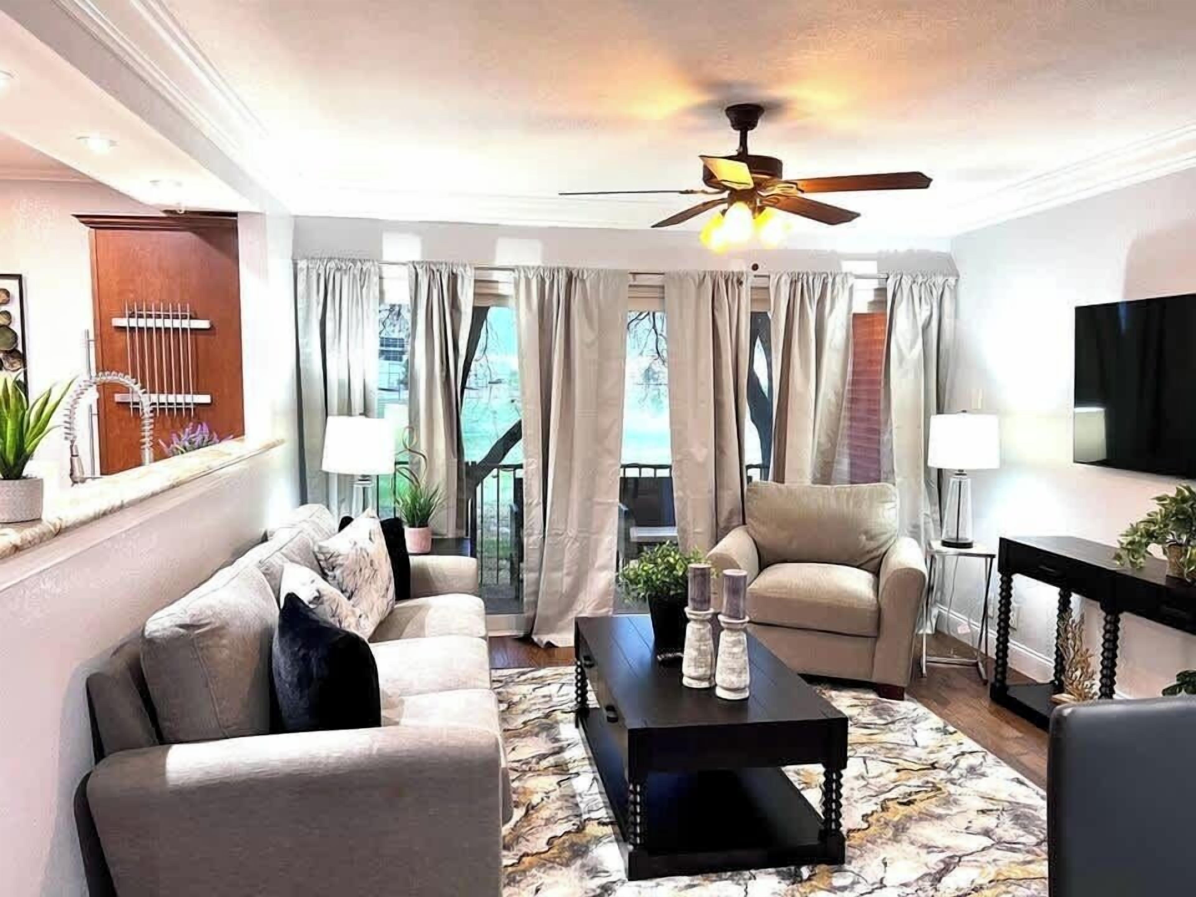 Una sala moderna con un sofá, un sillón, una mesa de centro y un ventilador de techo.