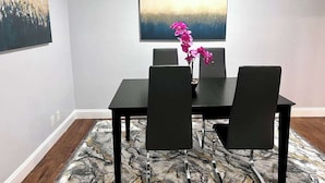 A dining area with a table and four chairs, a vase with pink flowers, and a painting on the wall. - Spacious  2BD Condo  HWY360/30  Grand Prairie (GP22B) (Grand Prairie)