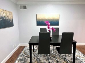Ein Essbereich mit Tisch und vier Stühlen, einer Vase mit rosa Blumen und einem Bild an der Wand.