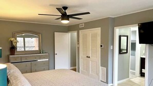 Ein Schlafzimmer mit Bett, Kommode, Deckenventilator und einer Tür zu einem Badezimmer.