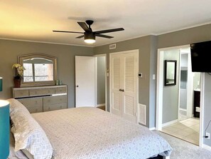 A bedroom with a bed, dresser, ceiling fan, and a door leading to a bathroom. - Modern 2BD Pool  Six Flags Grand Prairie GP08B (Grand Prairie)
