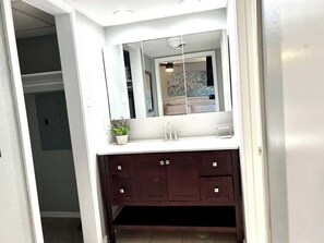 A bathroom with a white vanity, dark cabinets, a mirror, and a potted plant. - Modern 2BD Pool  Six Flags Grand Prairie GP08B (Grand Prairie)